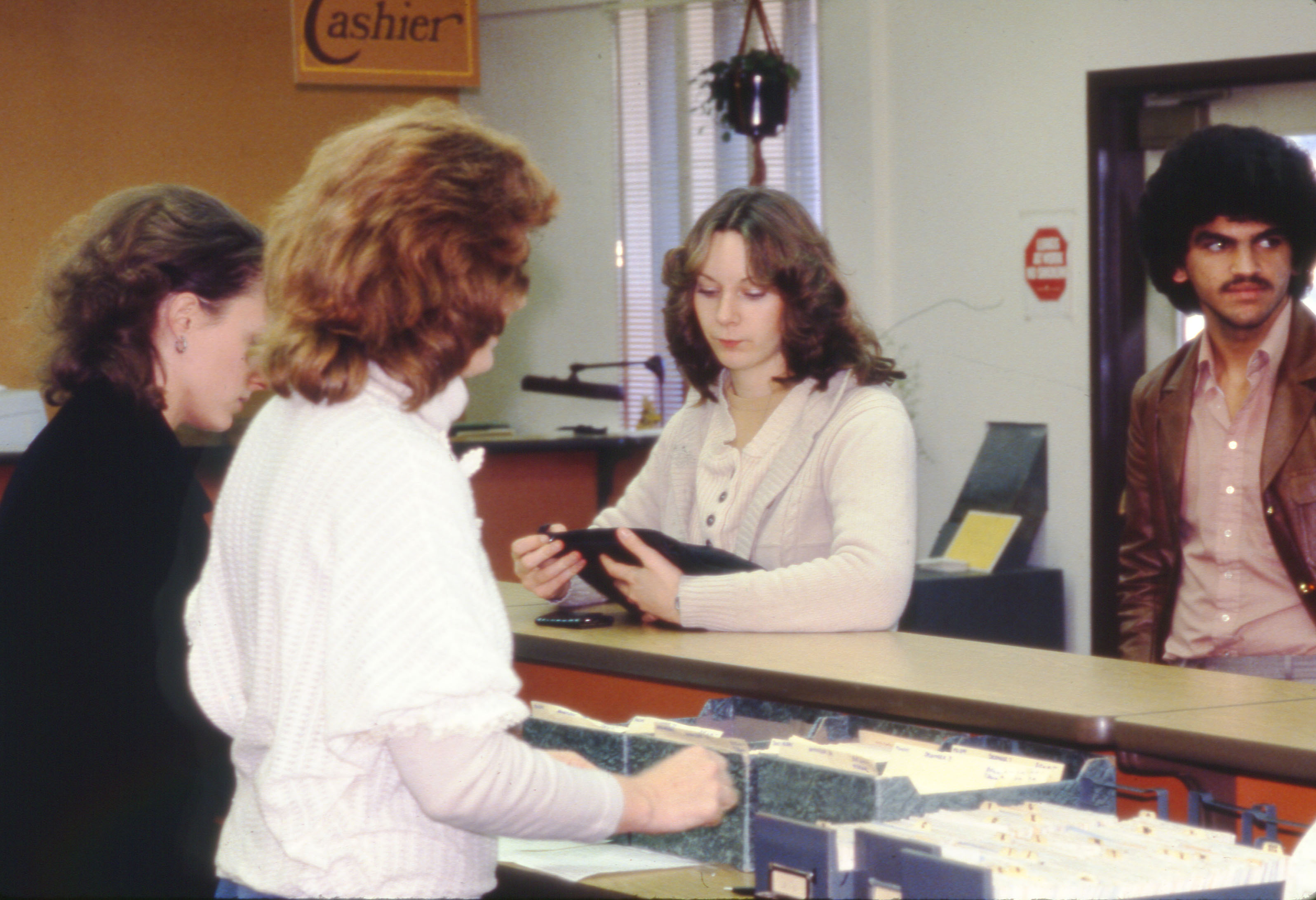 Two staff behind a desk serving two students with a Cashier sign in the background
