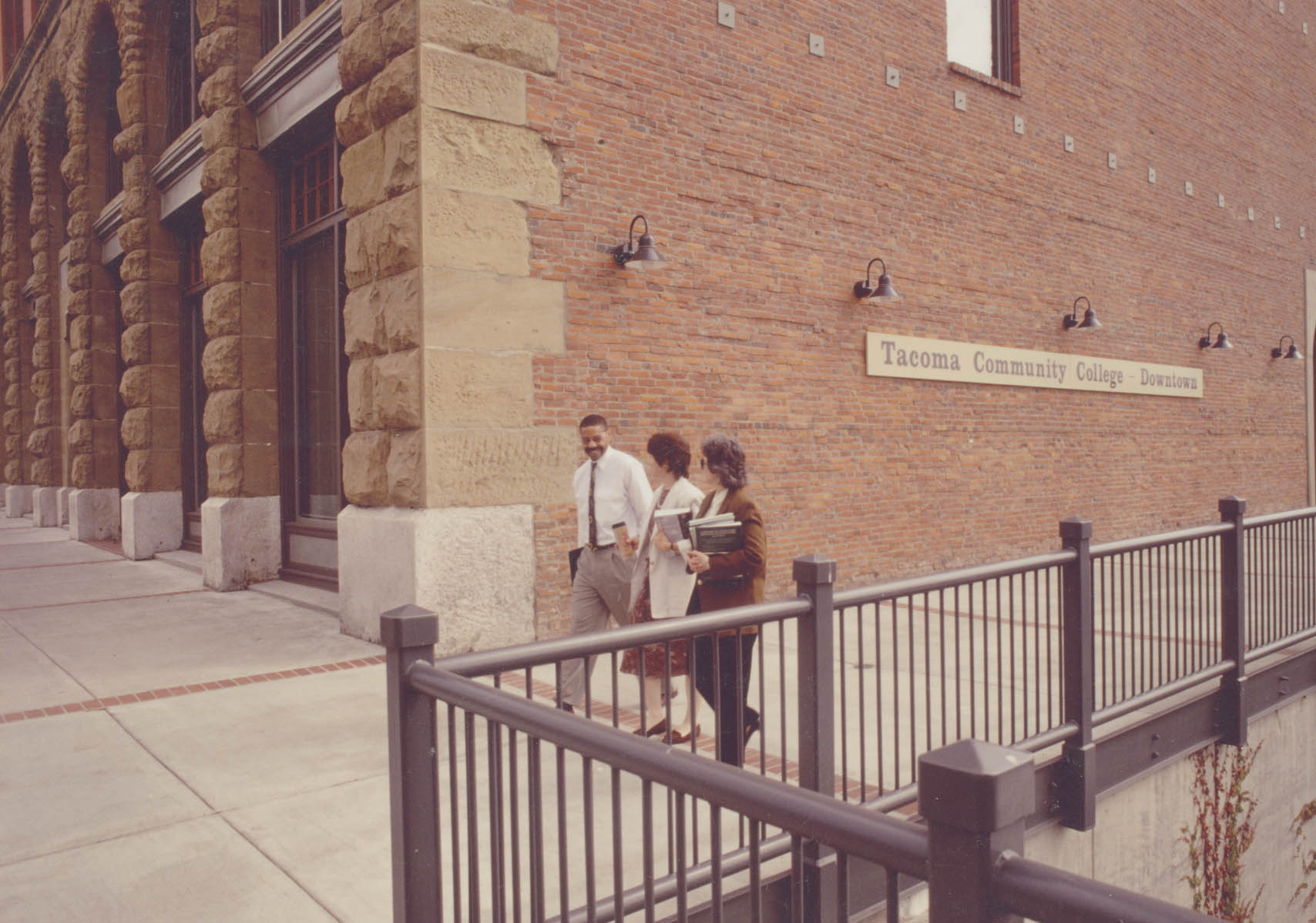 Three people walking in front of an exterior wall of the Downtown Center