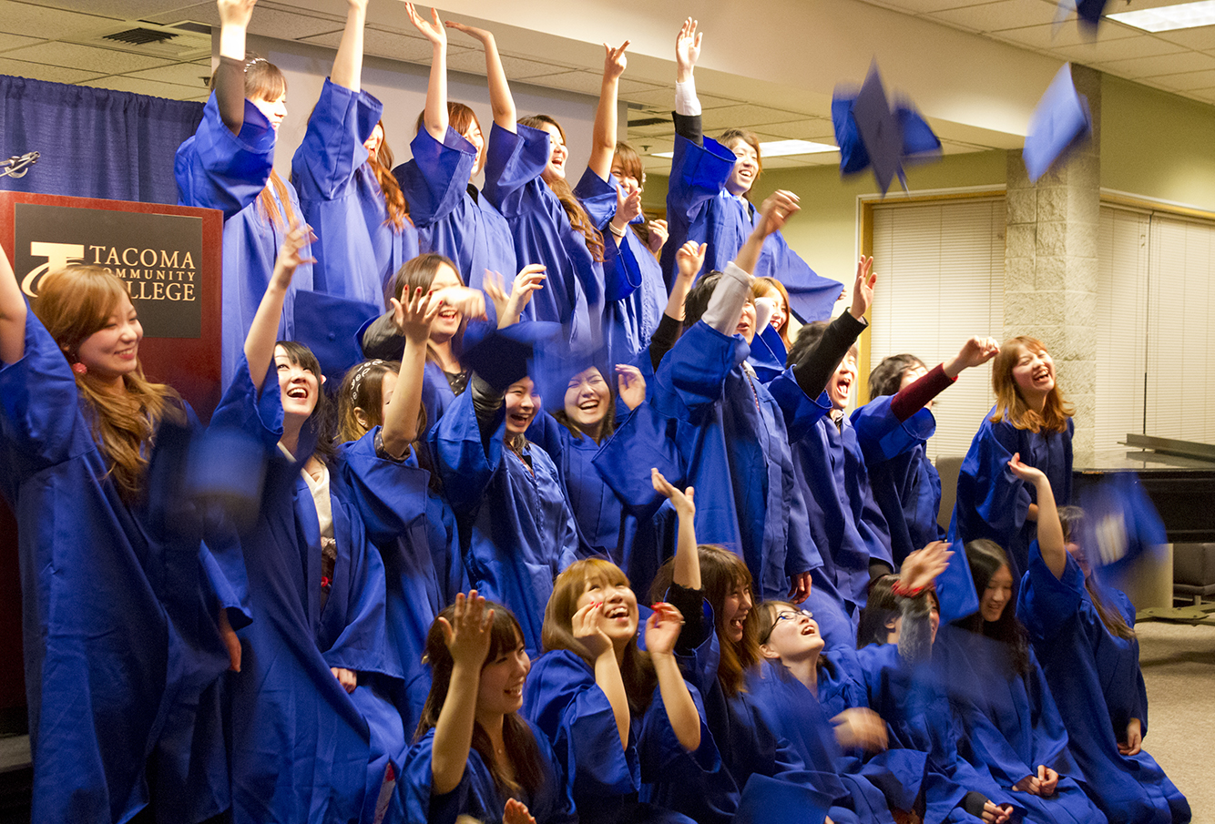 Japanese and Korean students in graduation regalia tossing their hats