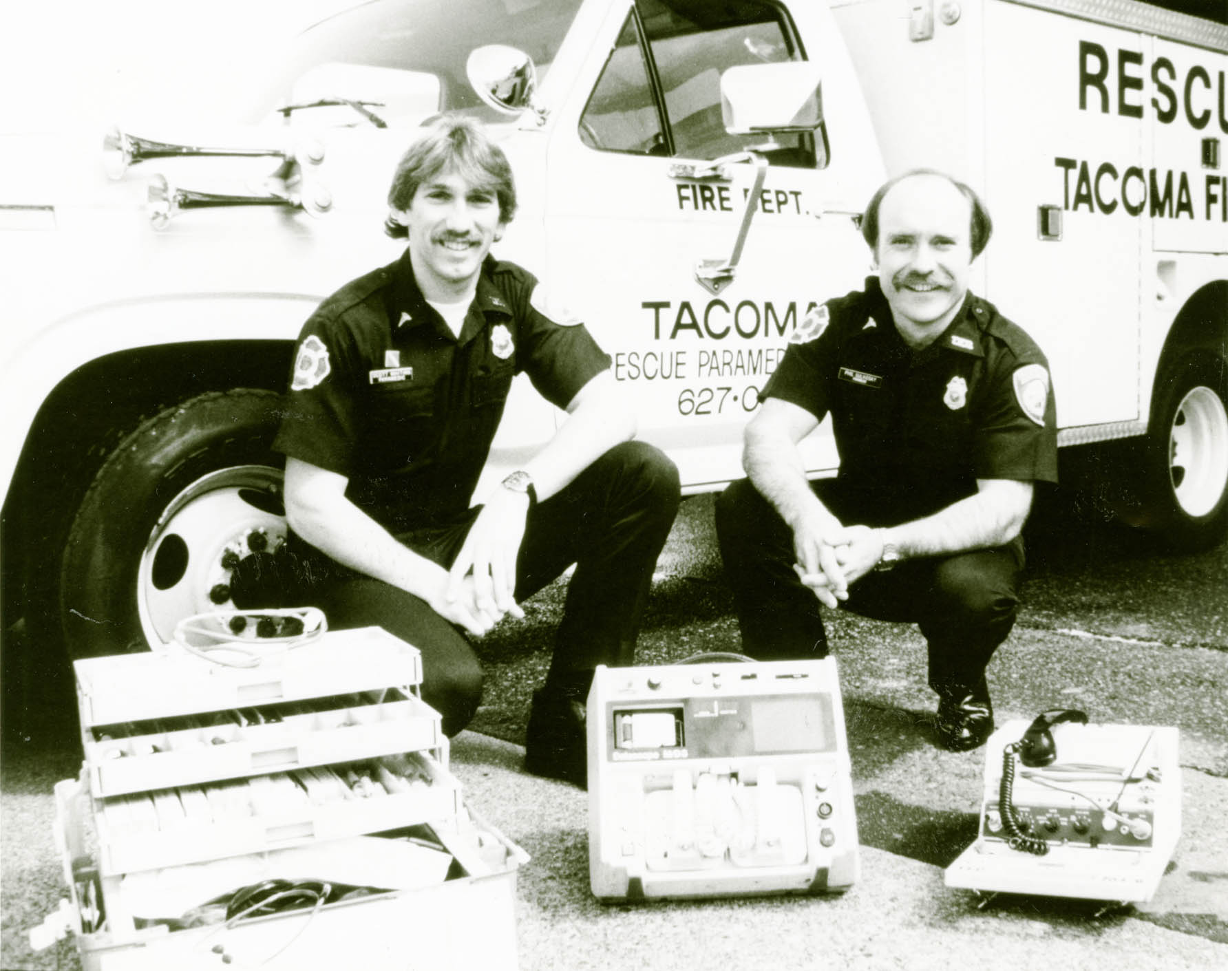 Two EMTs with equipment in front of vehicles
